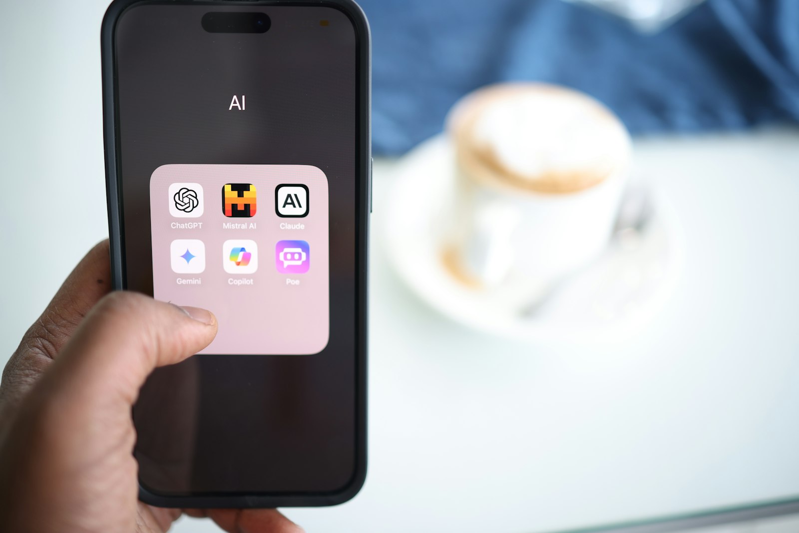 Mão segurando celular com apps de IA como ChatGPT, Gemini e Claude, foto real