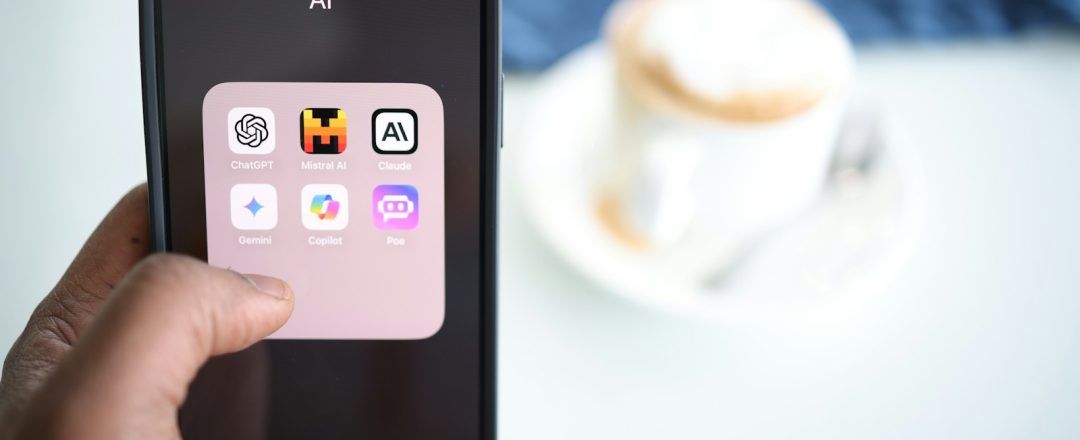 Mão segurando celular com apps de IA como ChatGPT, Gemini e Claude, foto real
